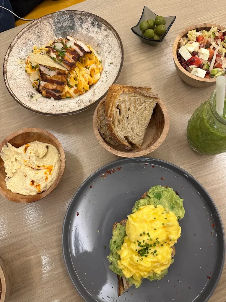 Brunch table with eggs on avocado toast, hummus, sourdough, salad, olives and a green juice